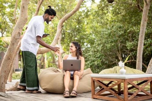 a man standing next to a woman sitting on a pillow with a laptop at Club Mango Resort in Kalpitiya