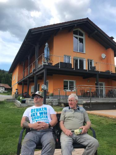 two men sitting on a bench in front of a building at Erlebnispension Zum Wanderer Sepp in Arnbruck
