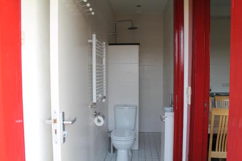 uma casa de banho com WC e uma porta vermelha em boerderij de duinen 113 em De Cocksdorp