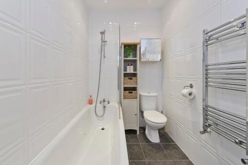 a white bathroom with a toilet and a bath tub at Veeve - East London Light in London