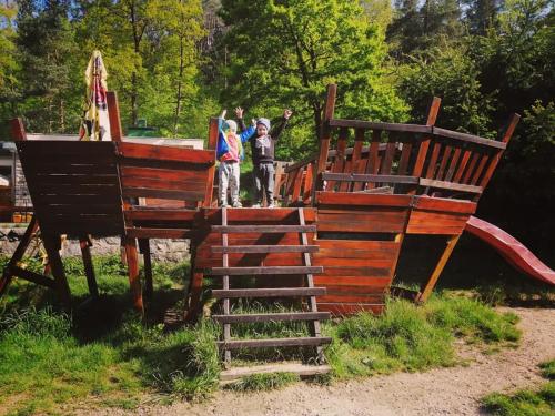 two children are standing on a wooden playground at Lesní Restaurace Harrachovka in Tábor