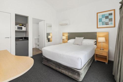 a bedroom with a white bed and a kitchen at Corrigans Cove in Batemans Bay