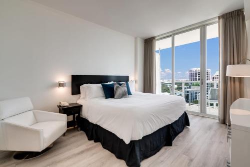 a bedroom with a bed and a chair and a large window at City View Balcony steps from Restaurants, Peacock Park & Marina in Miami