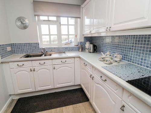 a kitchen with white cabinets and blue tiles at Coquet View Cottage in Morpeth