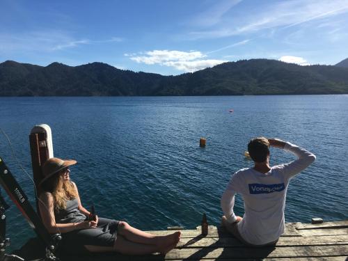 a man and a woman sitting on a dock by the water at Tawa Cove Cabins in Endeavour Inlet