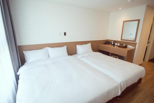 a large white bed in a room with a mirror at Kenny Stay Busan Gijang in Busan
