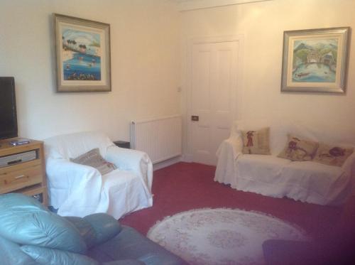 een woonkamer met 2 witte stoelen en een tv bij 250 yards from the Old Course and the town centre in St Andrews