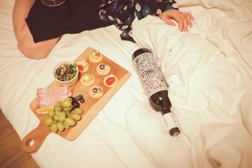 a person laying in bed with a bottle of wine and a tray of food at Kenny Stay Busan Gijang in Busan