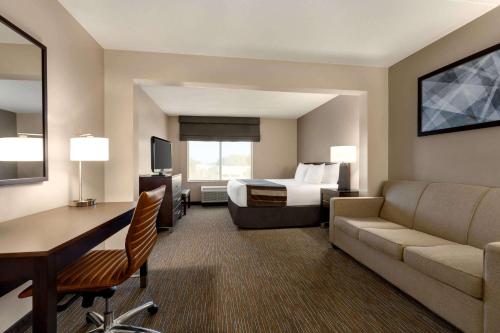 a hotel room with a bed and a couch and a desk at Wingate by Wyndham Wilmington in Wilmington