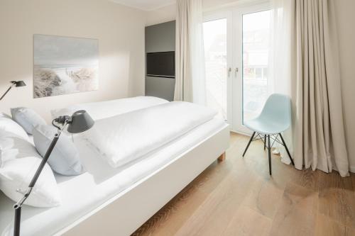 ein weißes Schlafzimmer mit einem weißen Bett und einem Stuhl in der Unterkunft meer suite juist 5 - mit Wattblick in Juist