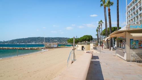 a beach with a building and palm trees and the ocean at Le Sun-Beach - Spacieux 3 pièces avec parking à 400 m des plages de Juan-les-Pins in Juan-les-Pins