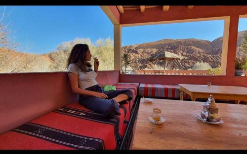 a woman sitting on a couch looking out a window at Auberge Kasbah Ait Marghad in Tamellalt