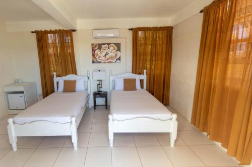 two beds in a room with two windows at St. James Guesthouse in Roseau