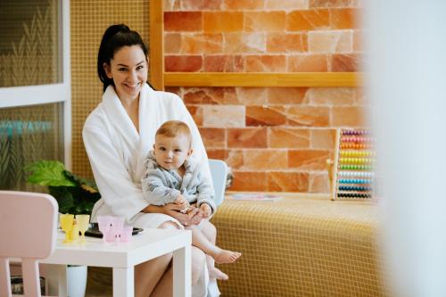 a woman in a bathrobe holding a baby at Elixír Medical Wellness Hotel in Mórahalom