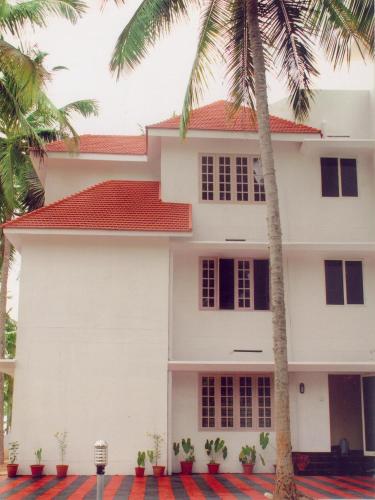 a white house with palm trees in front of it at Indeevaram Apartments in Kovalam
