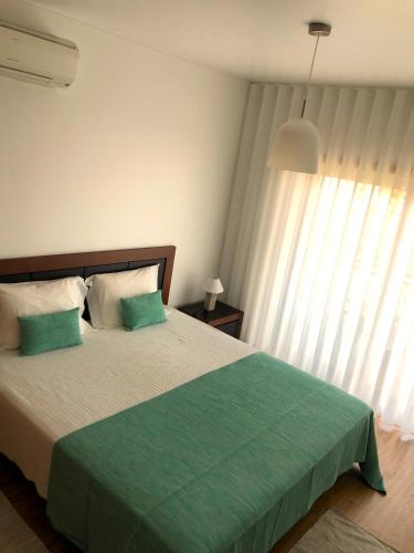 a bedroom with a large bed with green sheets and a window at Alojamentos Campo & Mar-T2 com Piscina in São Martinho do Porto