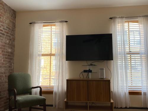 a living room with a flat screen tv and two windows at Riverhouse Extended Stay Apartment in Jersey City