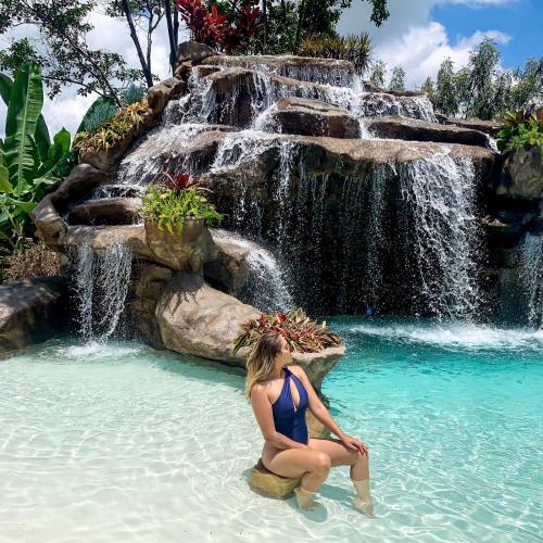 a woman sitting in the water in front of a waterfall at Lara's Home Suites in Capitólio