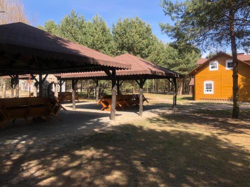 a pavilion with benches and a yellow house at Dolina Bobrów in Siennica