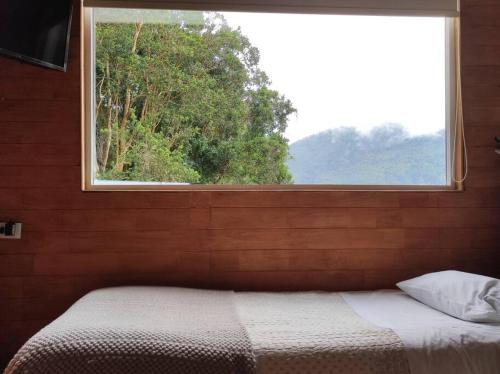Cama en habitación con ventana grande en Acogedora cabaña en el bosque, acceso solo vehiculos 4x4, en Cochamó