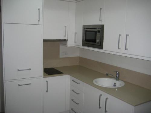 cocina blanca con fregadero y microondas en Apartamentos Fercamar Denia, en Denia