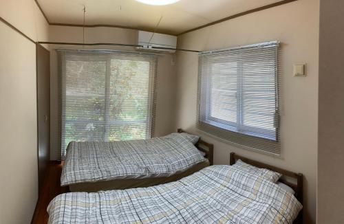 two beds in a bedroom with two windows at ゆくい家 in Ginowan