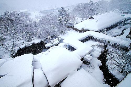 a yard covered in snow with a house and trees at Matsunoi in Minakami