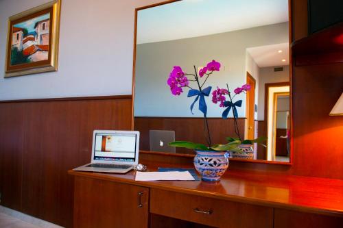 a desk with a laptop and a vase with flowers on it at Hotel Dei Pini in Porto Empedocle