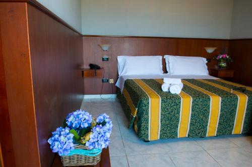 ポルト・エンペードクレにあるHotel Dei Piniのベッドルーム1室(青い花が入ったバスケット付)