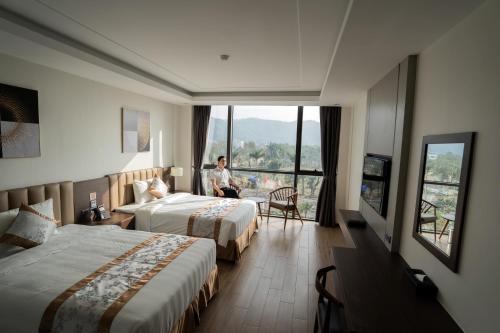 a man sitting in a chair in a hotel room with two beds at Songlam Waterfront Hotel - 藍江酒店 in Ha Tinh