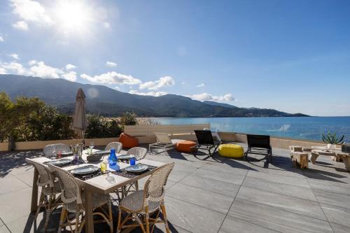 um pátio com uma mesa e cadeiras com vista para a água em La Maison sur la Plage em Calcatoggio