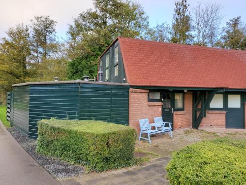 a green house with a red roof and a bench at Luxe vakantiehuisje in prachtige en rustgevende omgeving in Nieuwe-Niedorp