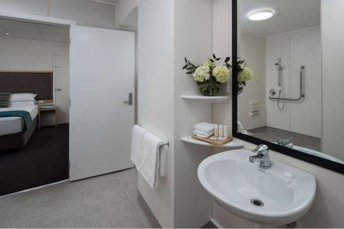 a bathroom with a sink and a mirror and a bed at Atura Wellington in Wellington