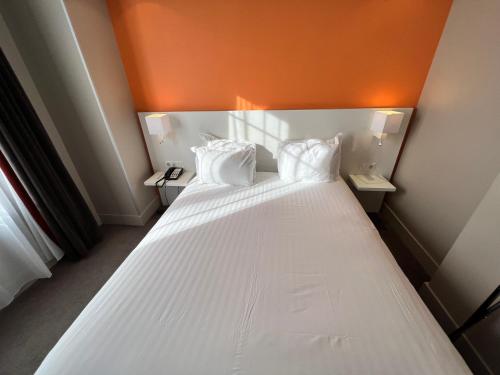 a large white bed in a room with an orange wall at Holiday Inn Paris-Auteuil by IHG in Paris