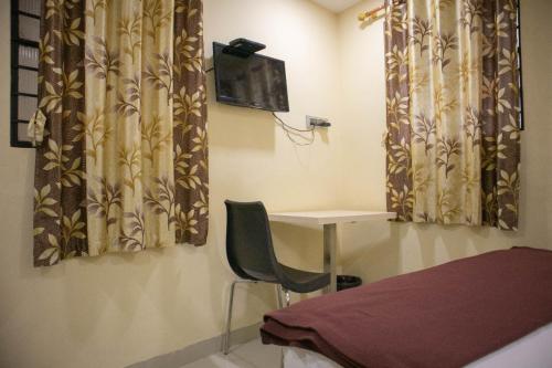 a bedroom with a chair and a desk and curtains at Shri Vasant Lodge in Hubli
