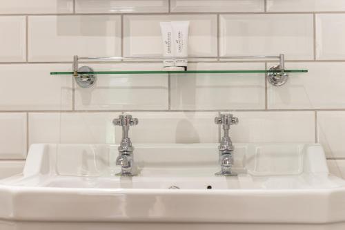 lavabo con 2 grifos y estante de cristal en Parva Farmhouse Riverside Guesthouse, en Tintern