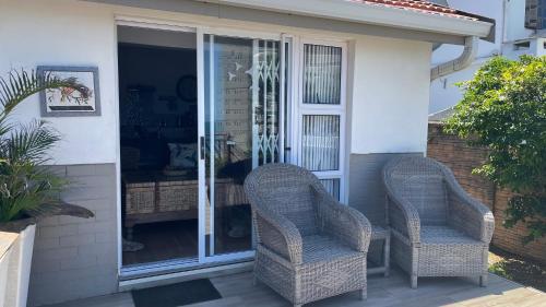 two wicker chairs sitting on the front porch of a house at Victorian Beach Cottages in Amanzimtoti