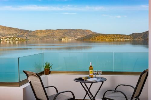 a table with two chairs and a bottle of wine on a balcony at Elounda Harmony Sea front apartment in Elounda