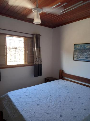 a bedroom with a bed with a ceiling fan and a window at Casa Aconchegante in São Sebastião