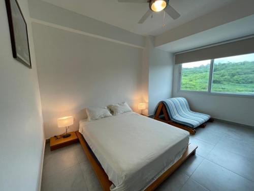 1 dormitorio con cama, ventana y silla en Departamento vista al mar 2D, en Tonsupa