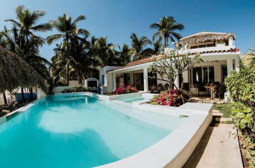 a swimming pool in front of a house with palm trees at Villa Rincon del Mar & Villa Rincon de las Morenas in Coyuca