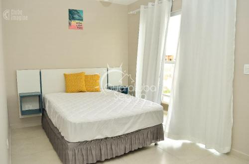 Un dormitorio blanco con una cama con almohadas amarillas y una ventana en Sobrado PôrDoSol2 Aconchegante 4 suítes pertodomar, en Guaratuba