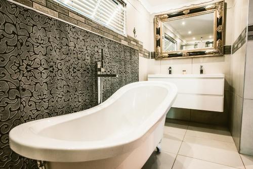 a white bath tub in a bathroom with a mirror at Le Grant Guesthhouse in Kroonstad