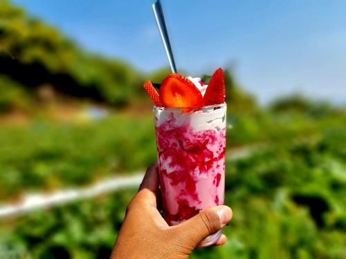 a hand holding a drink with a strawberry on it at DV INNS FARMVILLA - Besides Strawberry Farms in Mahabaleshwar