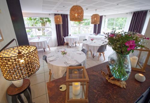 un comedor con mesas blancas y un jarrón de flores en Hotel Au Bon Coin du Lac, en Mimizan