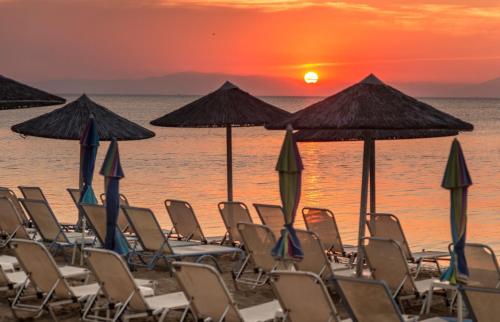 a group of chairs and umbrellas on the beach at sunset at Eantos Studios and Suites in Perea