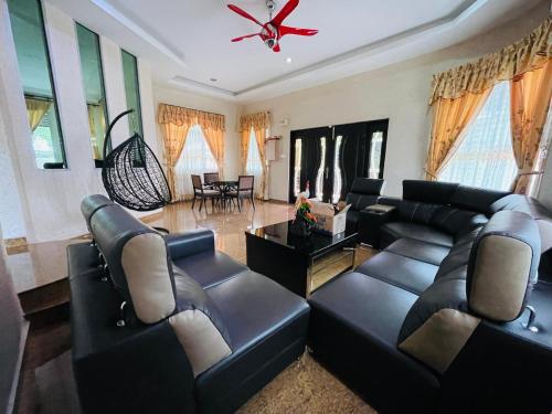 a living room with black leather furniture and a ceiling fan at Homestay Seri Pangkor in Pangkor