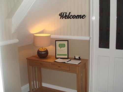 a table with a lamp and a welcome sign on the wall at The Fawley Guest house in Shanklin