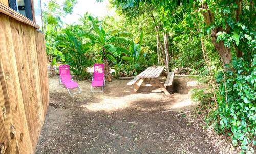 a picnic table and two pink chairs next to a fence at LODGE COLIBRIS Piscine Privée vue panoramique mer et montagne pelée , 500 m plage dans un parc , Calme assuré Idéal pour découvrir le nord Caraïbes in Le Carbet