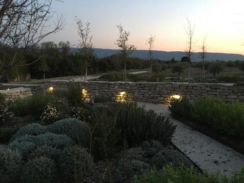 einen Garten bei Sonnenuntergang mit einer Steinmauer und Lichtern in der Unterkunft Ferme Oleicole Les Callis in Gordes